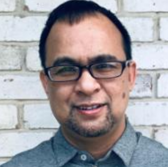 A headshot of Professor Long Le. He is wearing glasses and a grey shirt and standing in front of a white brick wall.