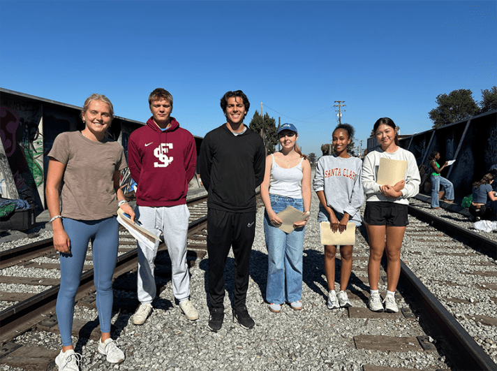 A group of students standing on the railroad tracks where unhoused people are camped.