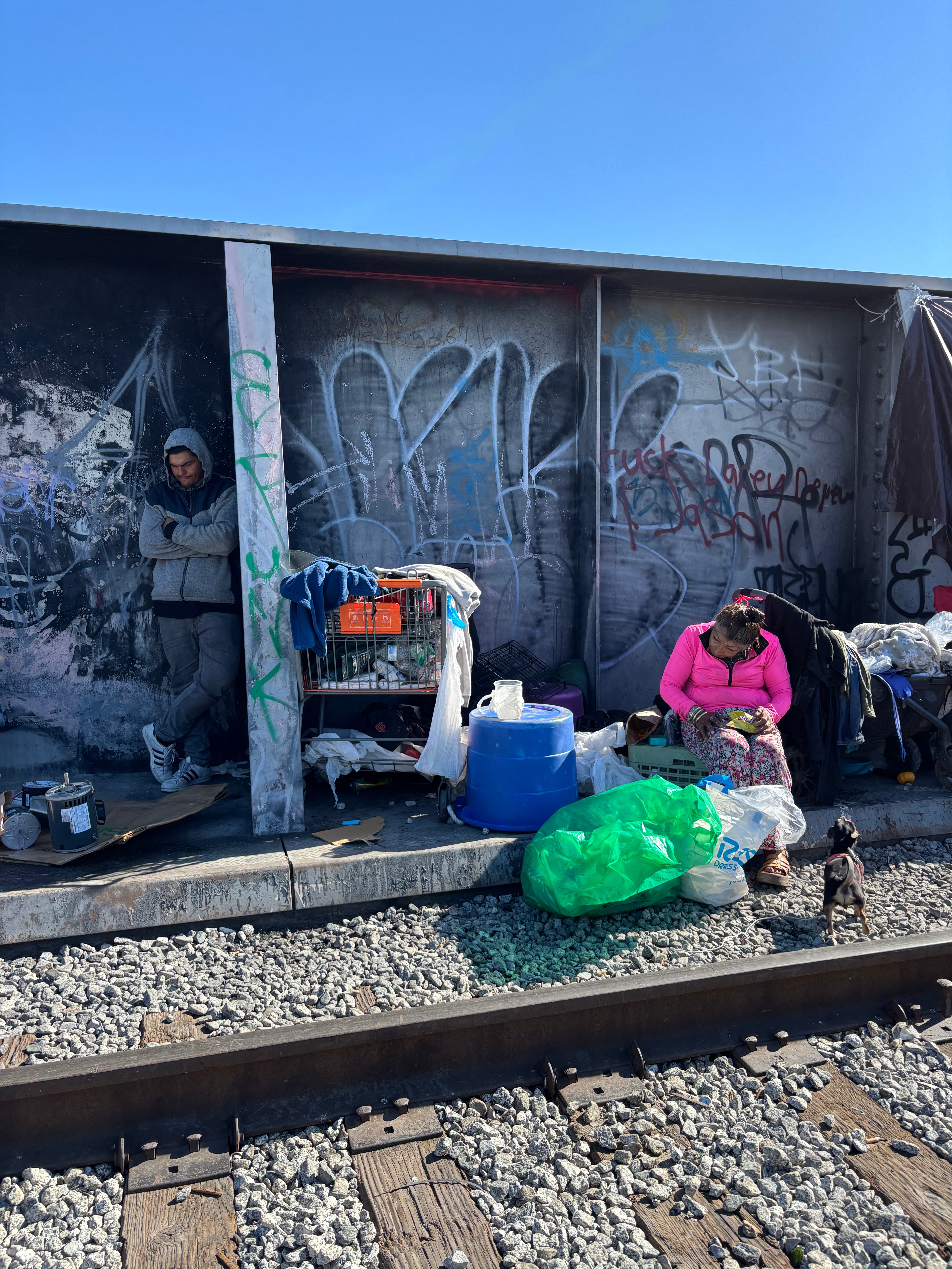 two people pictured in their encampment adjacent to railroad tracks.